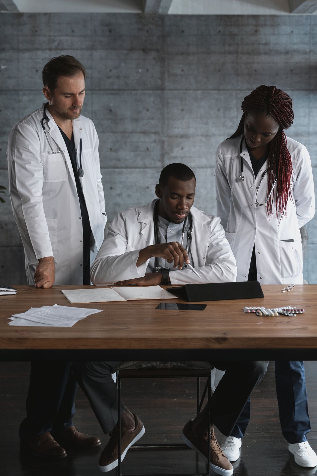 Three doctors in white coats reviewing notes at a table
